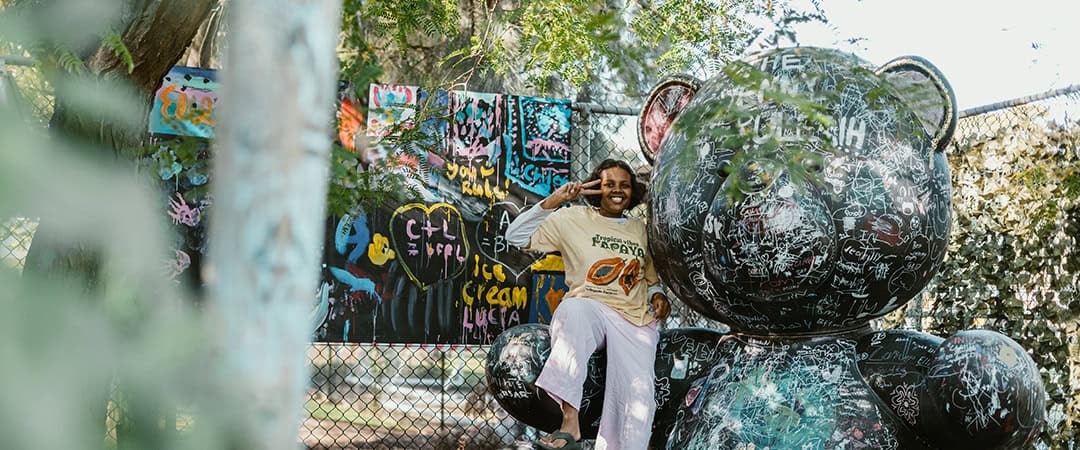 A young girl sitting on a large, artistic bear sculpture at The Venny community space, surrounded by.