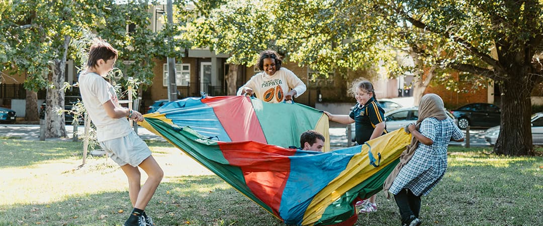 Children playing with colorful parachute in a sunny park at The Venny community farm.